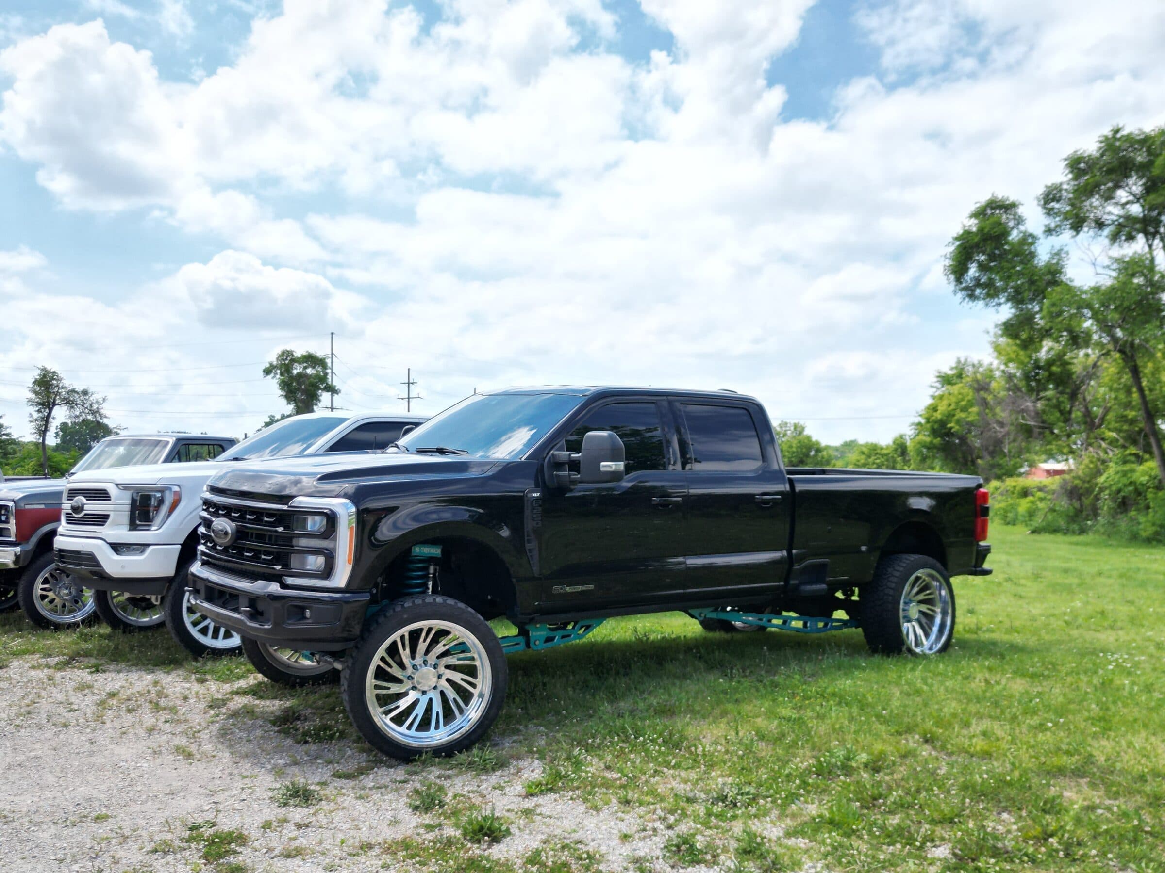 Lifted black Ford Super Duty on polished forged wheels, parked on grass outside the shop